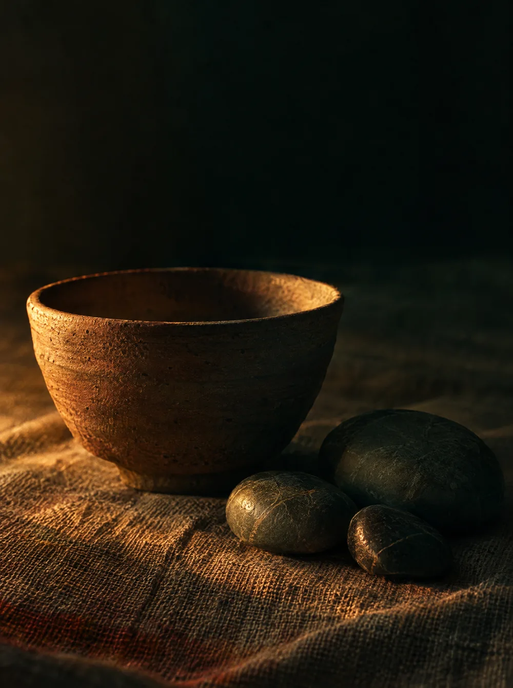 An unglazed clay tea bowl and river stones on linen